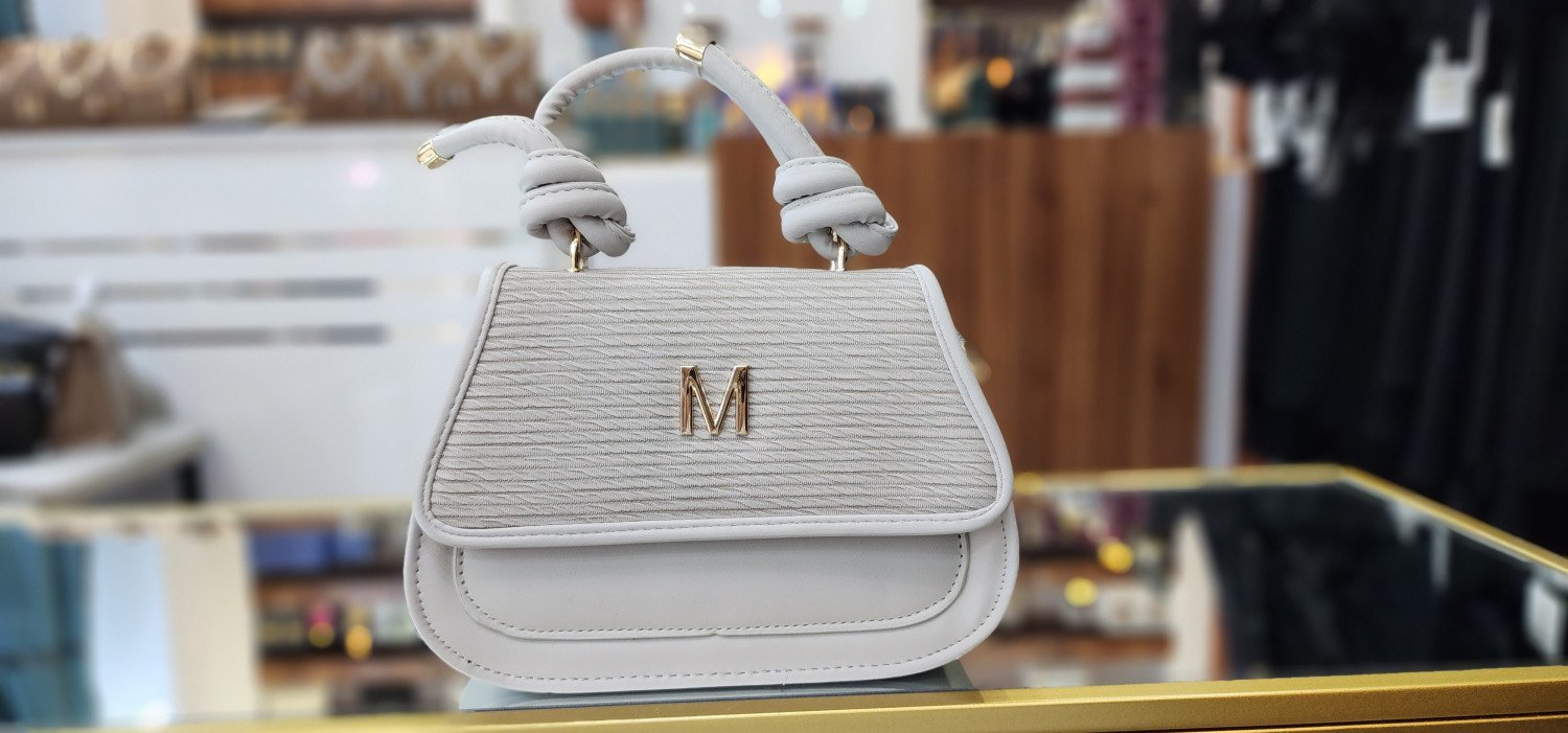 حقيبة يد نسائية بيضاء اللون مزينة بحرفM باللون الذهبي